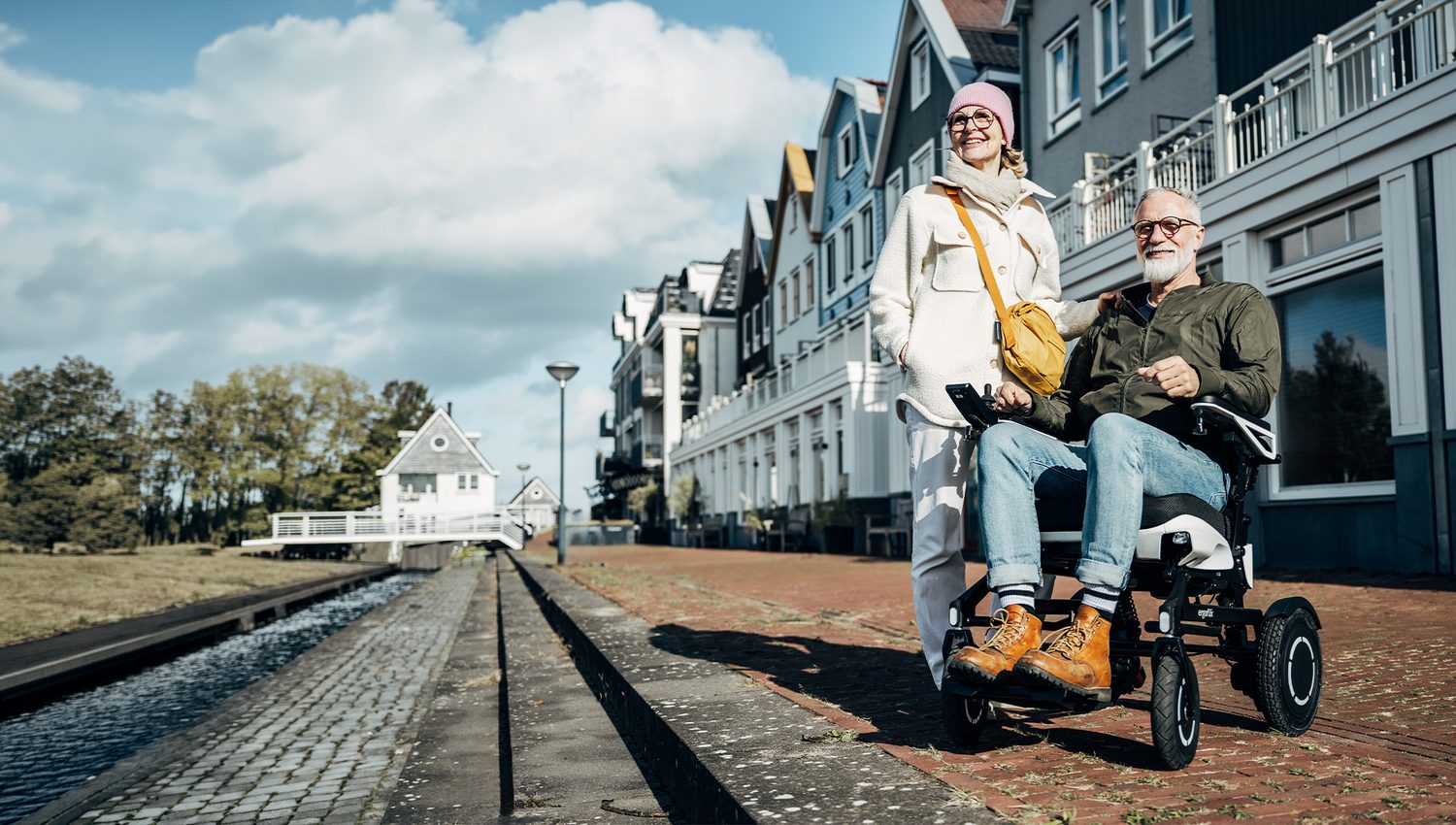Ein Senior fährt im ergoflix vario an einem Kanal entlang, seine Partnerin begleitet ihn.